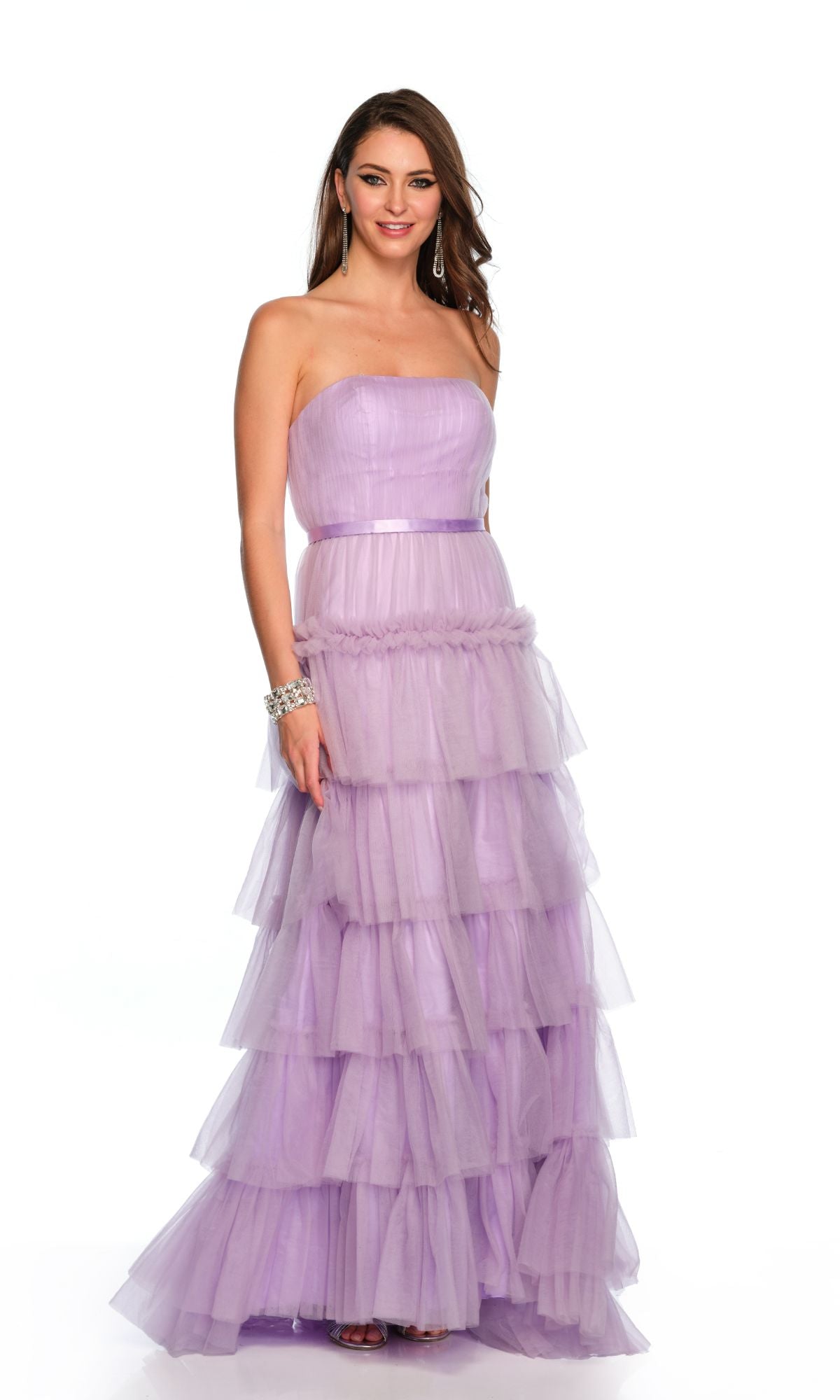 A woman wearing the Long Formal Dress 11579 by Dave and Johnny, a floor-length lilac purple strapless A-line tulle dress with layered ruffles, stands against a plain white background.